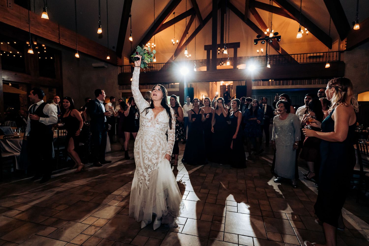 Guest in white gown celebrating on dance floor surrounded by cheering crowd.