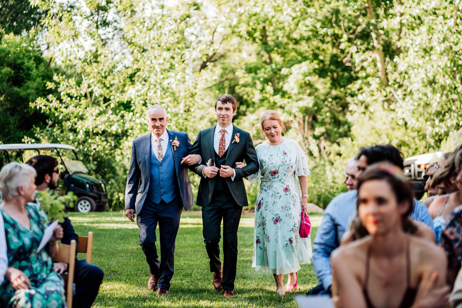 Wedding party members walking down an outdoor aisle during a garden ceremony.