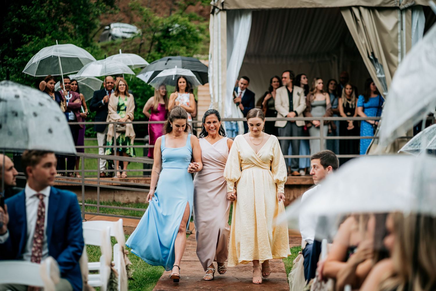 Wedding guests with umbrellas walking down a path during a rainy outdoor ceremony.