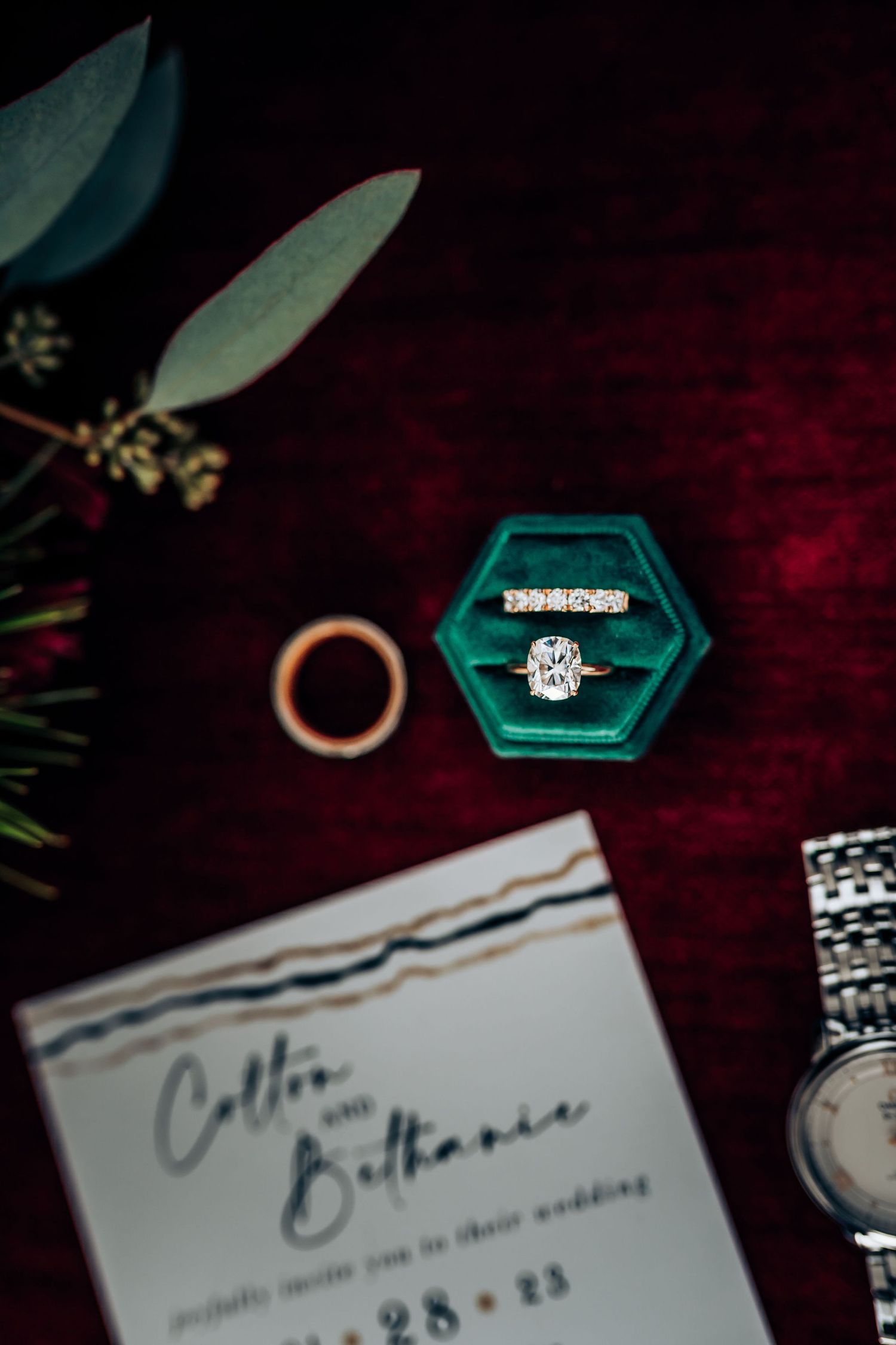 Engagement ring in teal hexagon box with wedding invitation and floral decor.