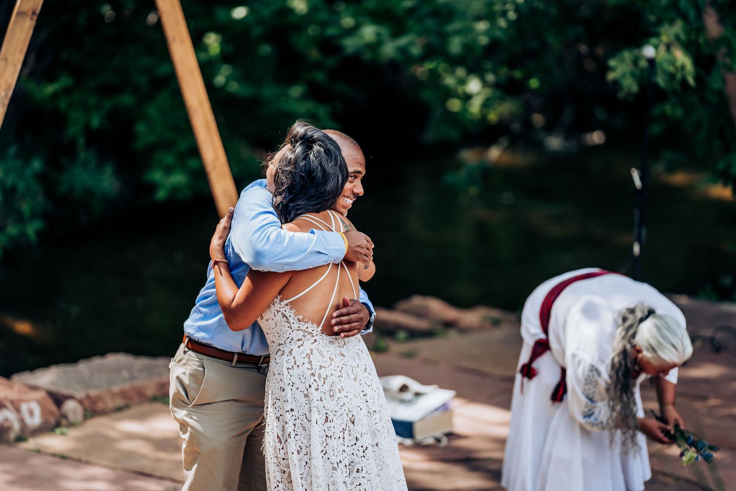 An emotional embrace during an outdoor celebration with floral arrangements nearby.