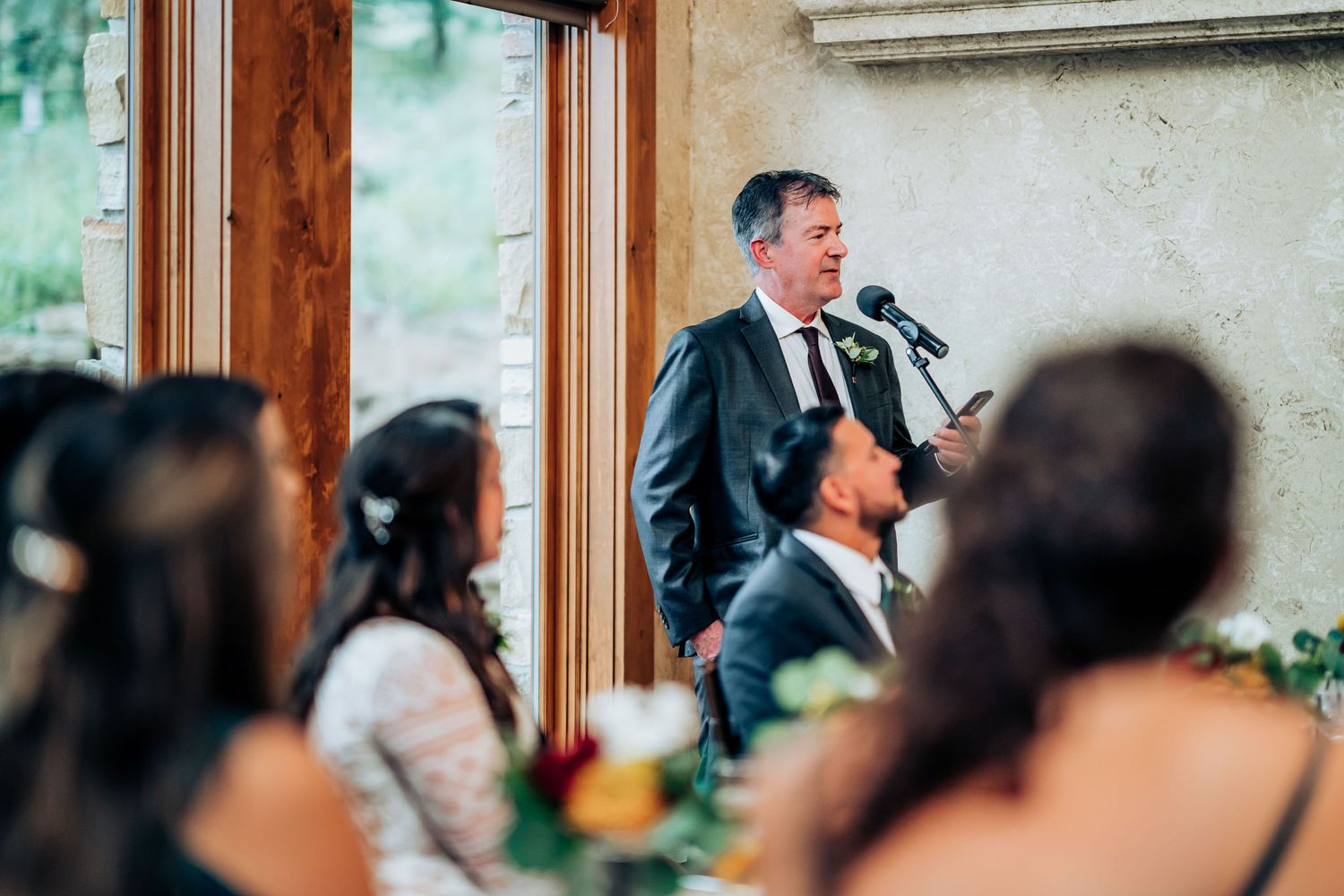 Speaker giving a toast at an elegant wedding reception near large windows.