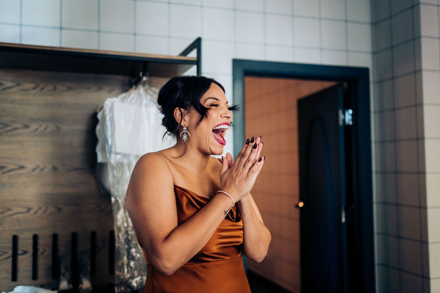 A wedding guest in a brown dress expressing joyful excitement in a hotel room.