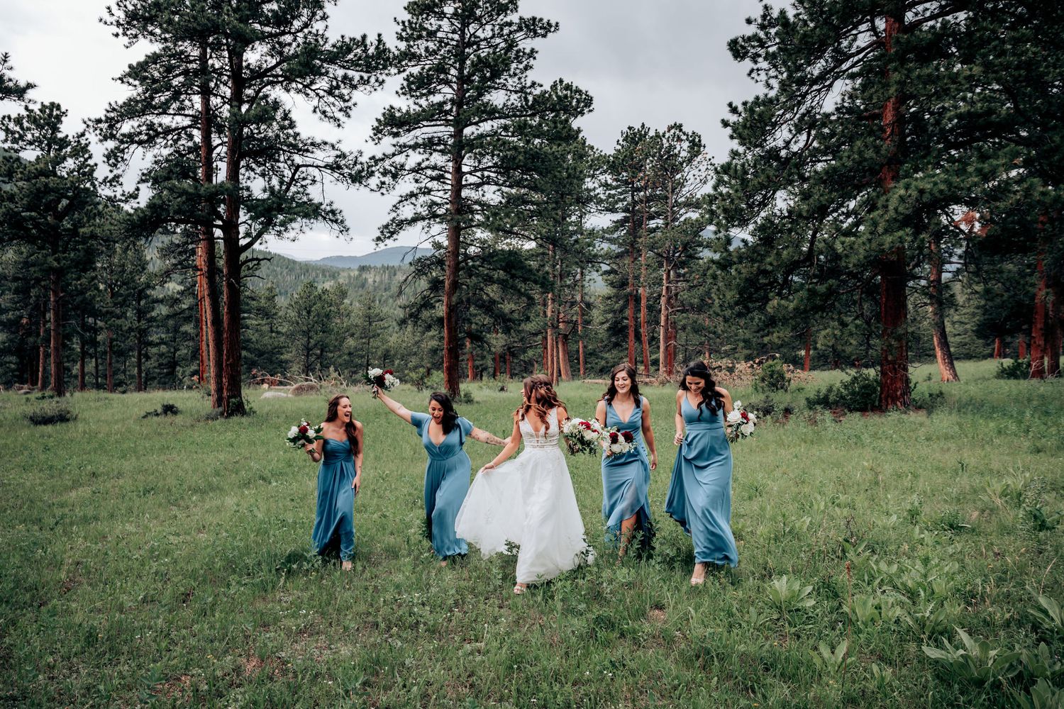 Bridal party dances and celebrates in an outdoor forest setting with mountain views.