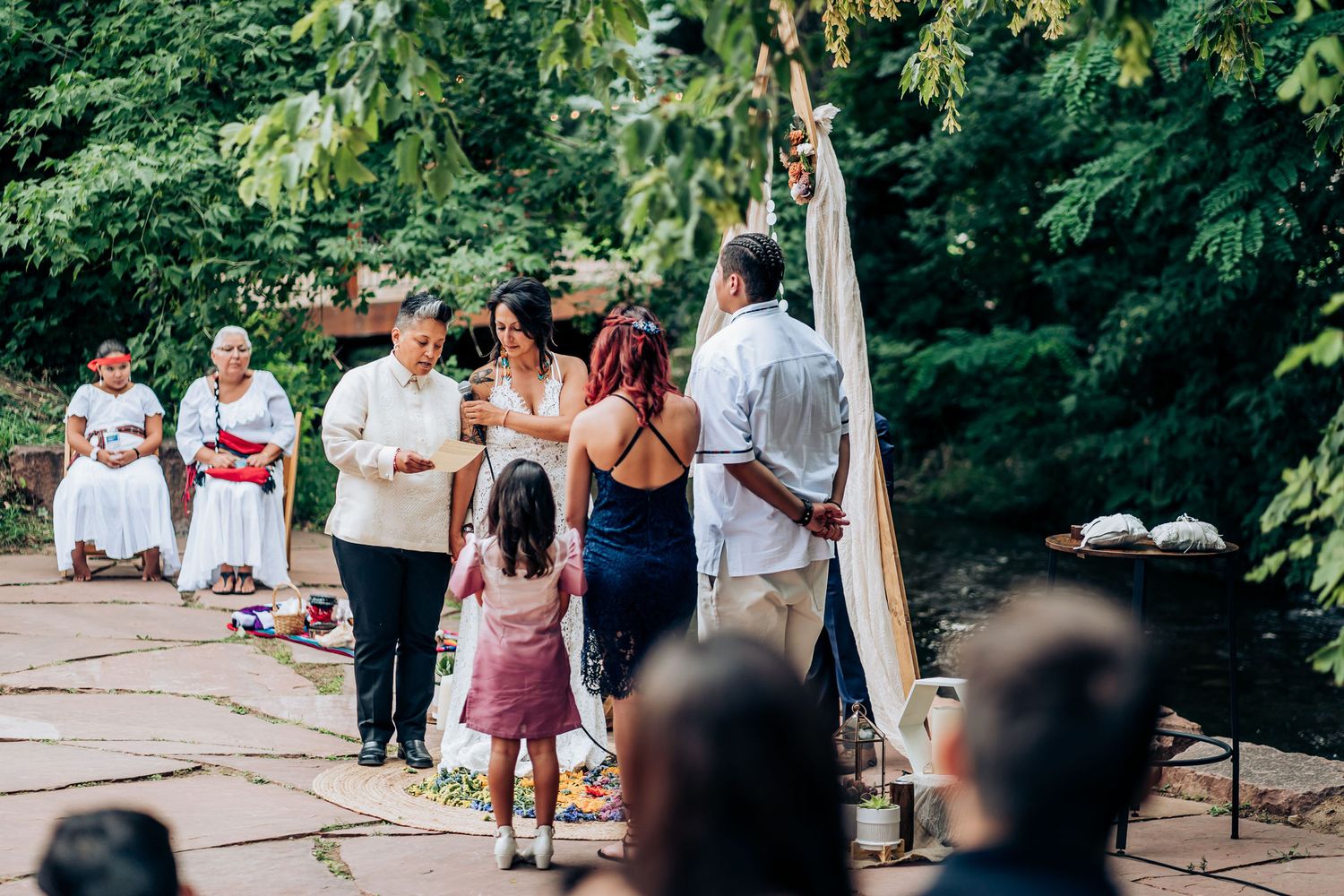 Small outdoor wedding ceremony with people gathered around a wooden triangle arch.
