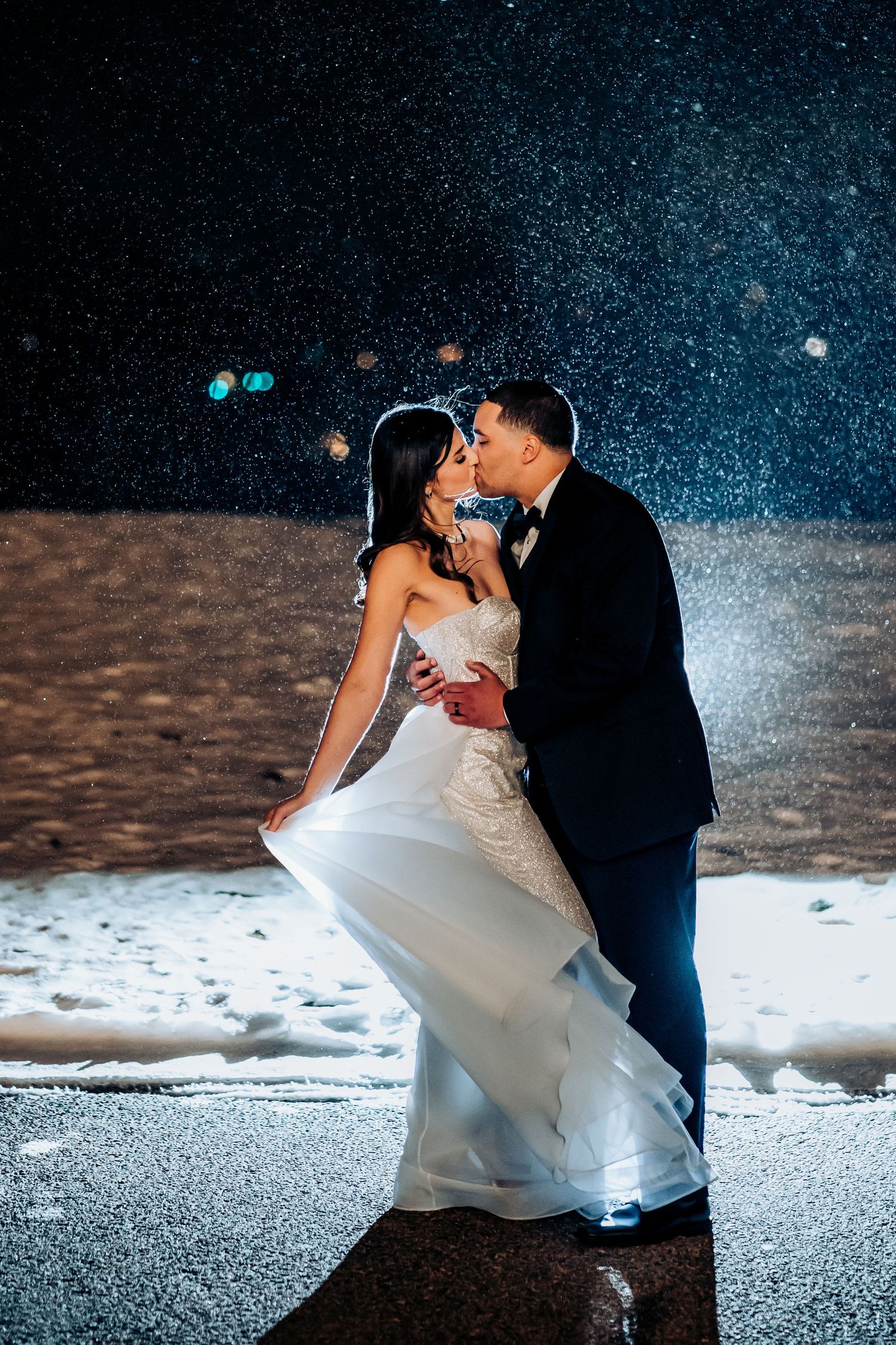 Romantic nighttime winter wedding portrait with snow and twinkling lights.