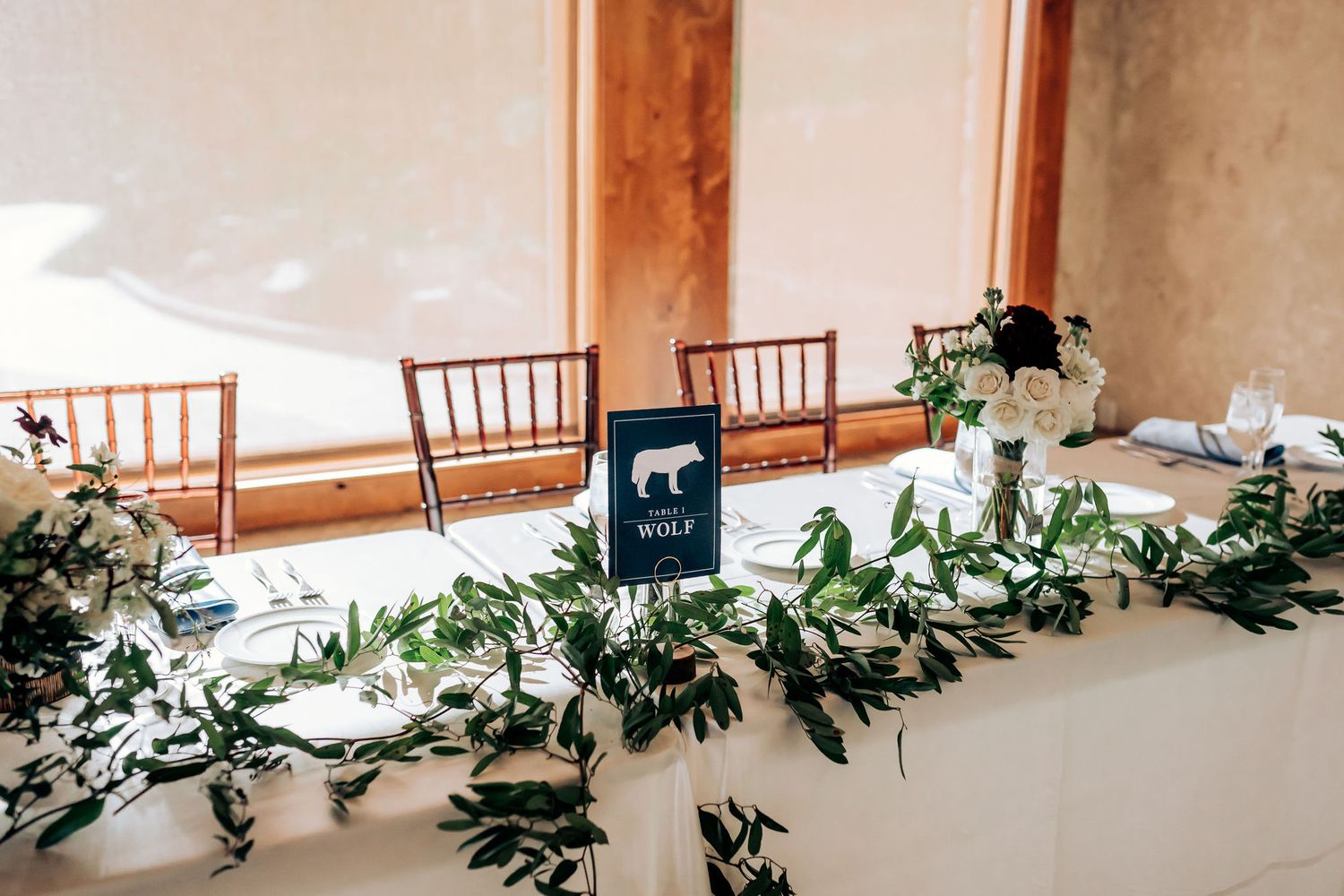 Elegant wedding reception table with greenery garland and small chalkboard sign displayed.