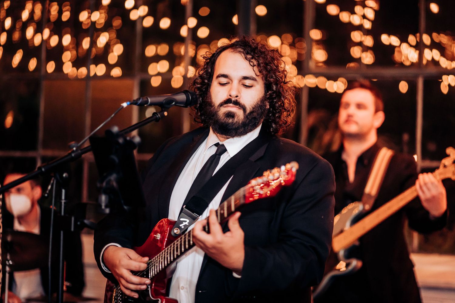 Wedding band guitarist performs under atmospheric string lights at evening reception.