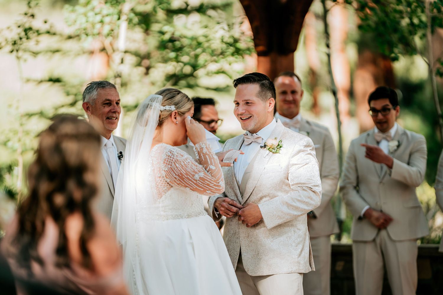 Wedding ceremony moment under trees with couple exchanging vows.