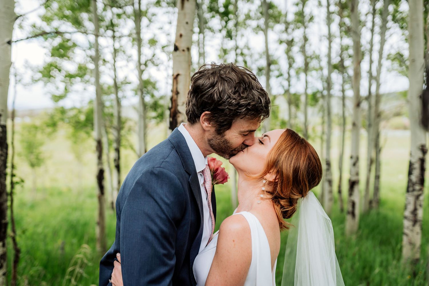 Romantic kiss shared between newlyweds in a spring aspen grove.