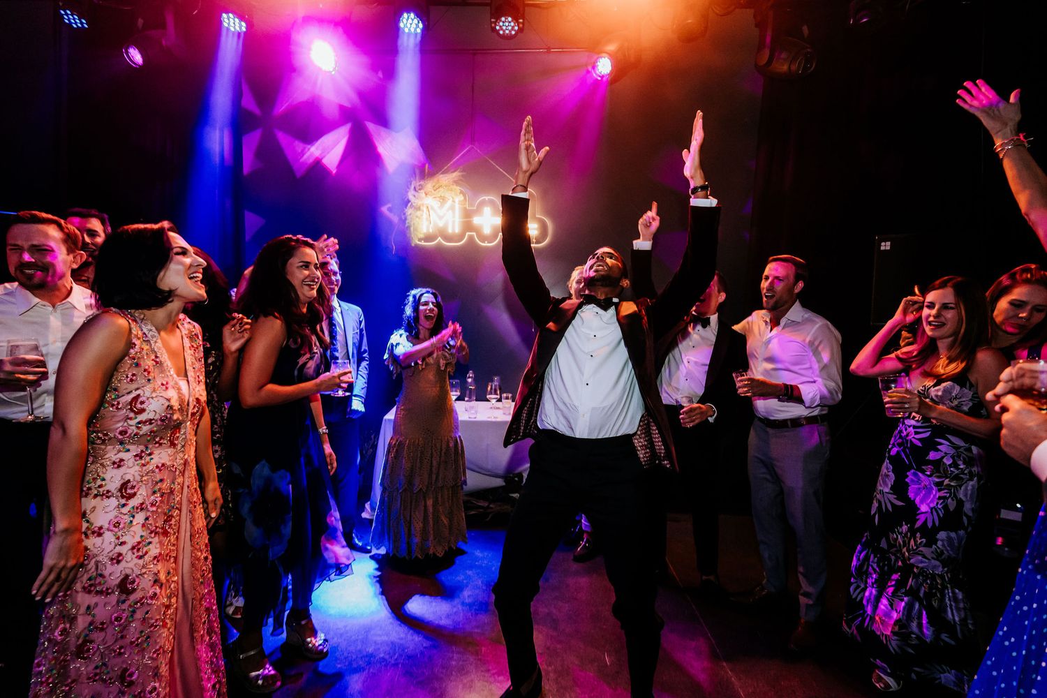 Energetic dance party with colorful lighting and guests raising hands in celebration.