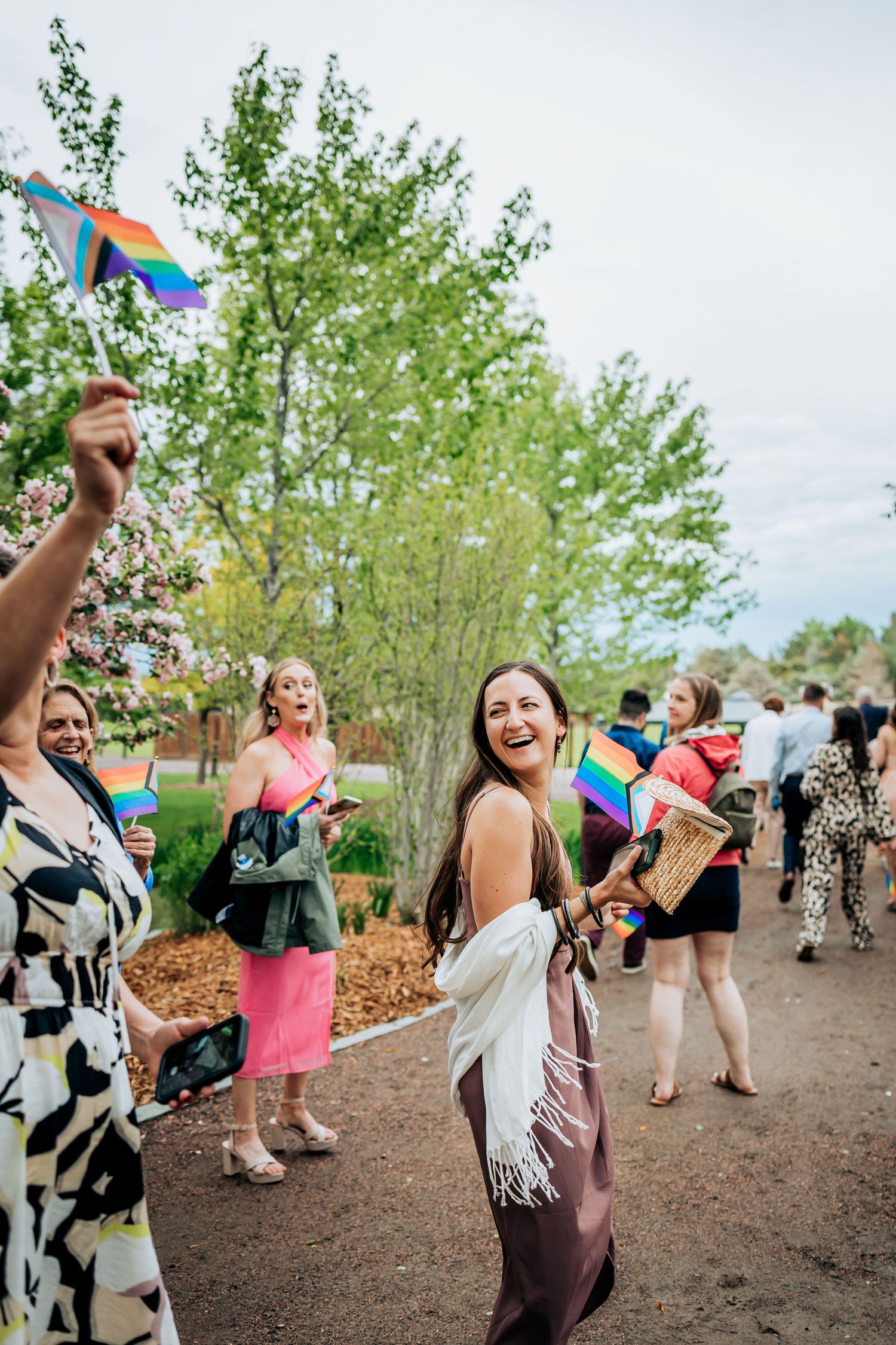 Wedding guests celebrating with rainbow flags and joyful expressions on garden path.