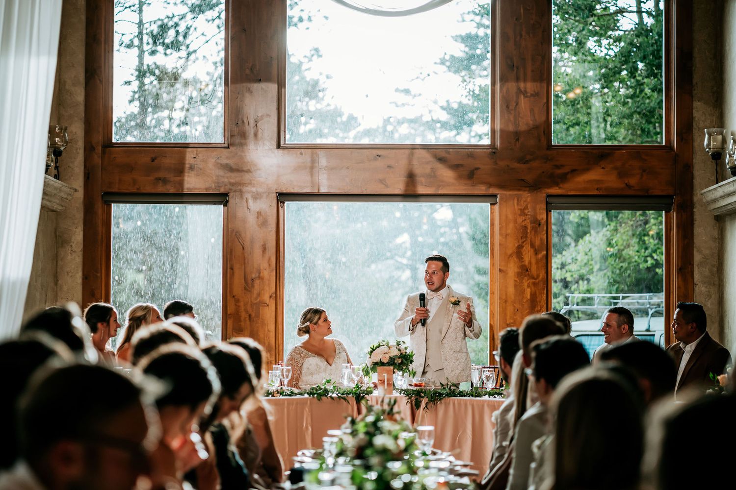 Wedding reception speech in a rustic venue with wooden beams and large windows.