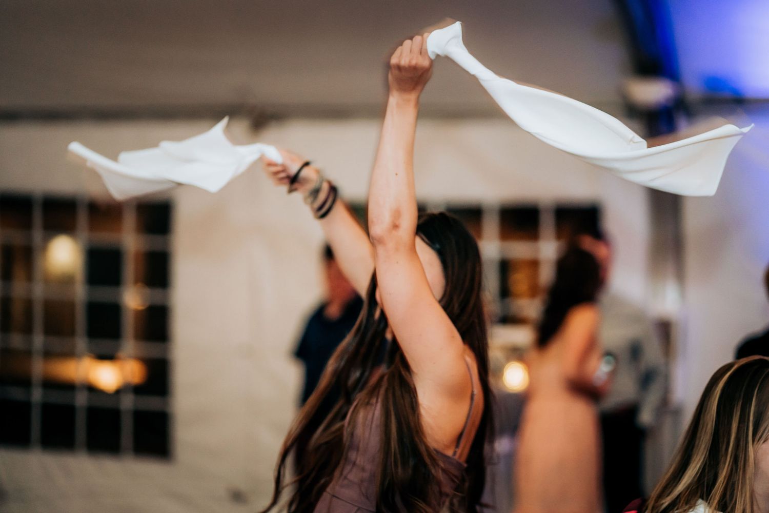 Person waving napkins enthusiastically during indoor celebration.