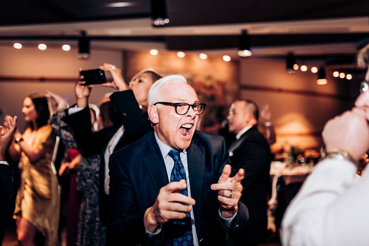 Wedding guests dancing and celebrating enthusiastically at an indoor reception.
