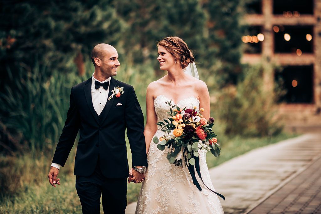 A couple walking together on a garden path at dusk with string lights in the background and lush greenery.