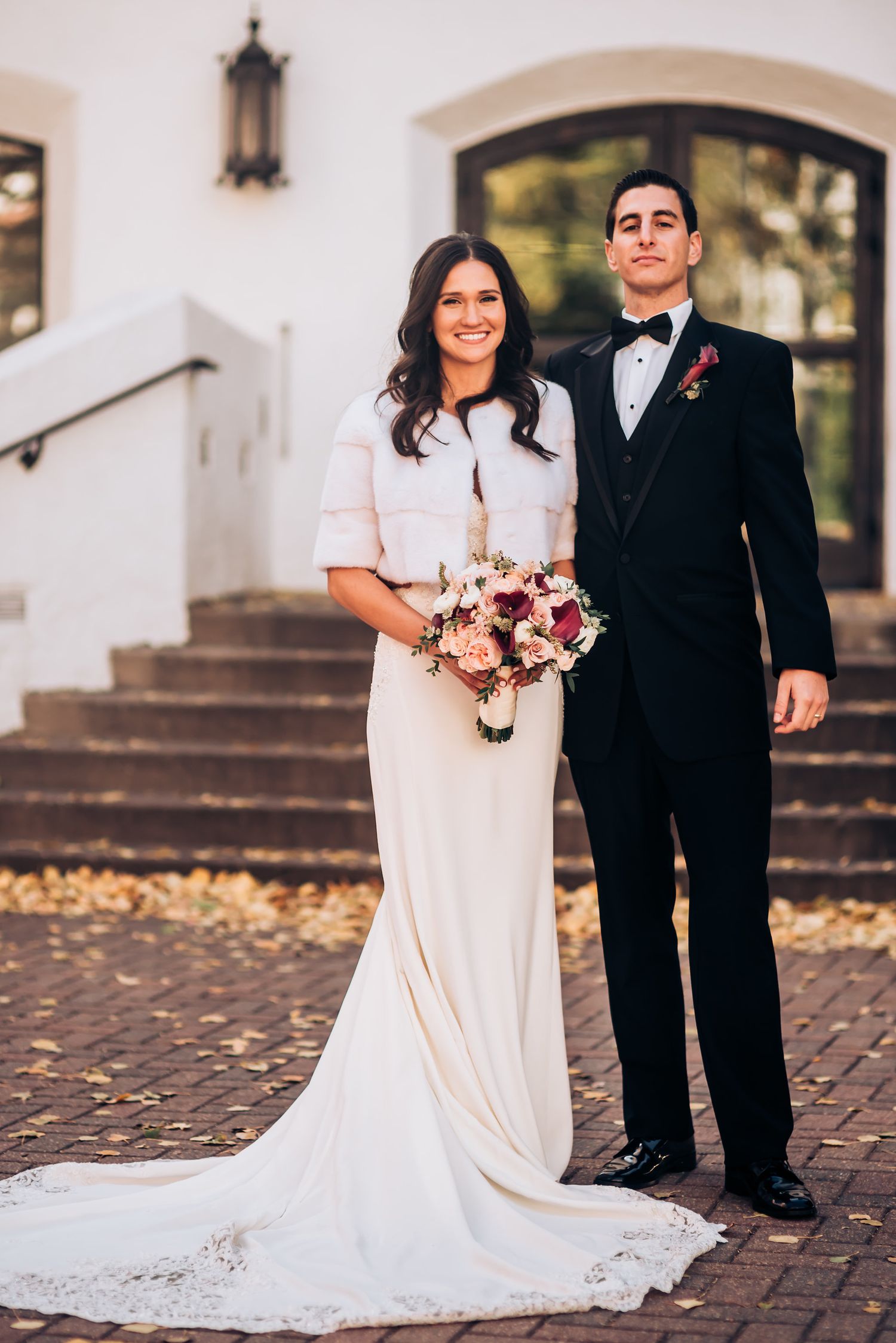 Wedding couple poses formally on brick steps in front of white church building.