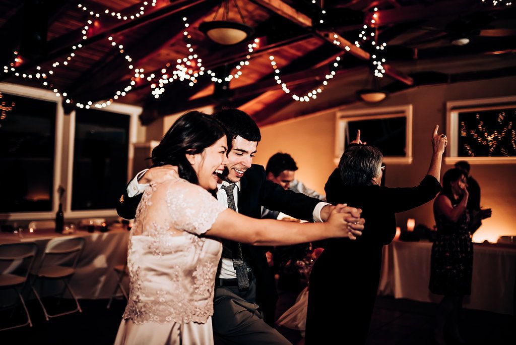 Reception guests dancing energetically under string lights and warm lighting.