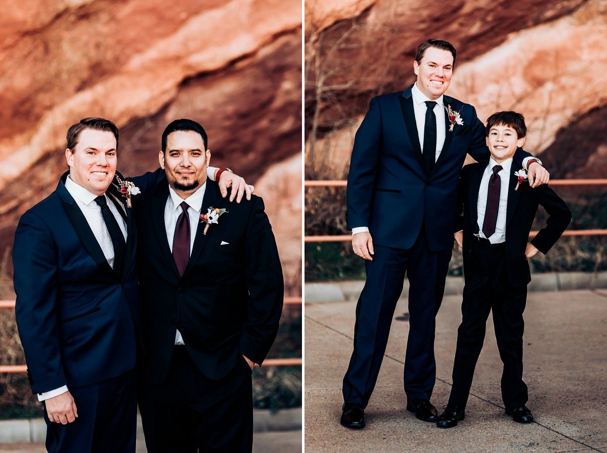 Wedding party members in dark suits pose against red rock formations outdoors.