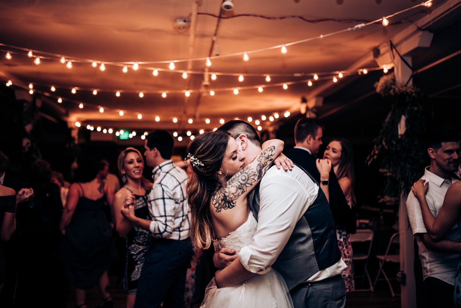Wedding reception dance floor filled with couples swaying under glowing string lights.