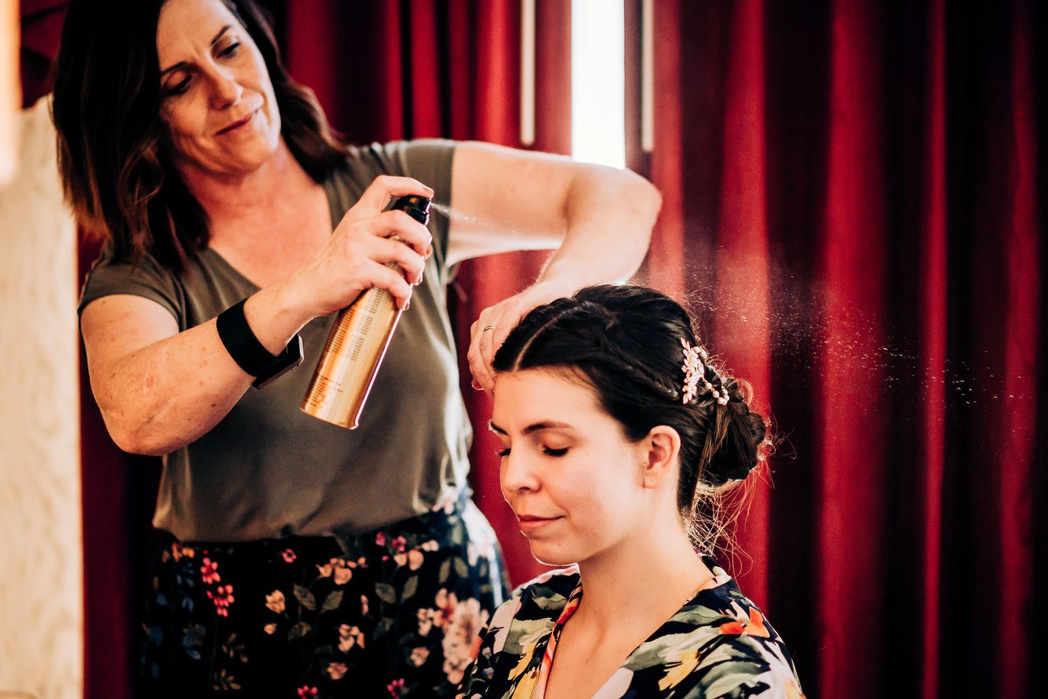 Hair styling preparation with hairspray in front of red curtains.