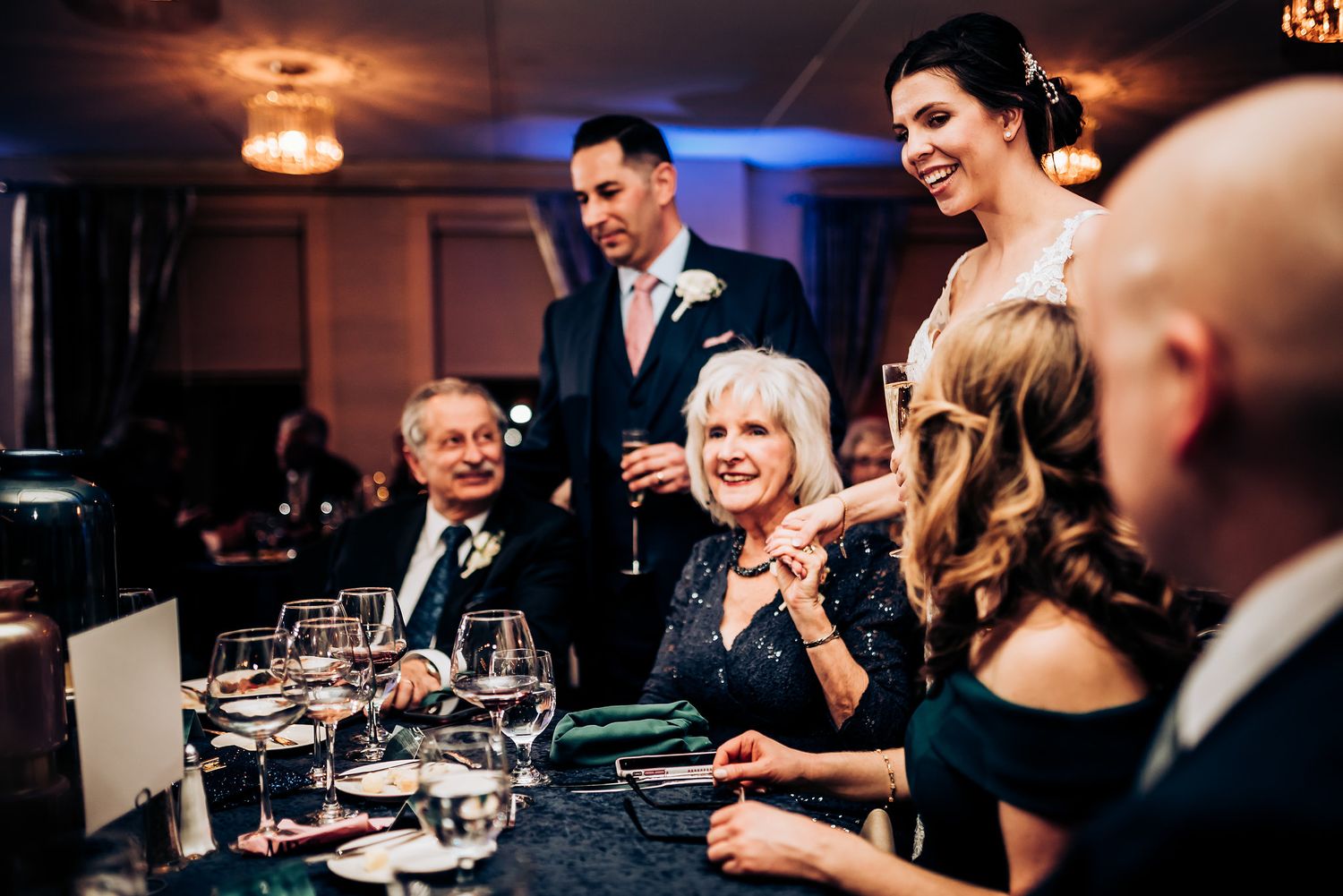 Wedding guests laugh and smile during a dinner reception at an elegant table setting.