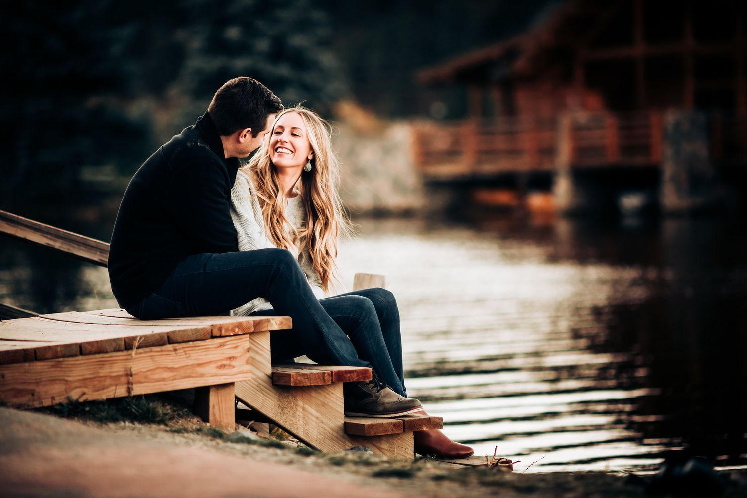 Couple sitting together on wooden dock steps by a lake during intimate outdoor photo session.