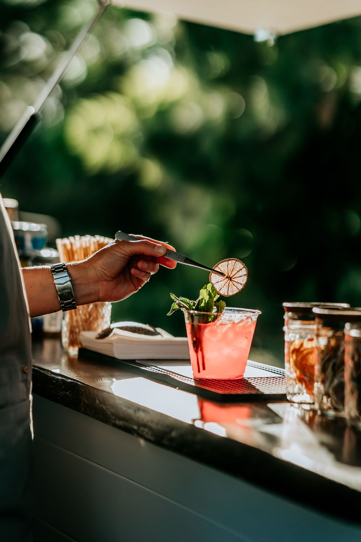 Colorful cocktails being prepared at an outdoor bar with garnishes.