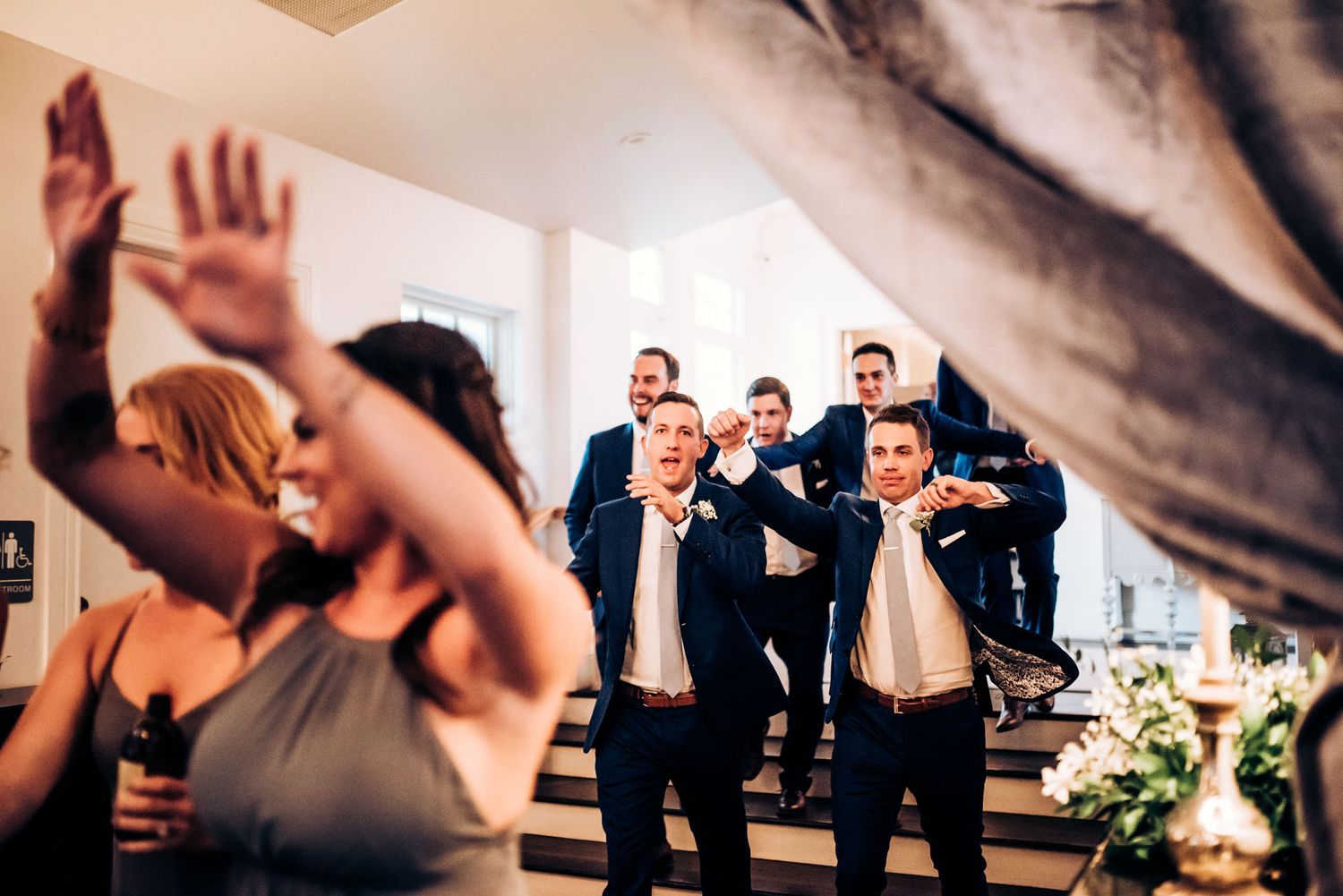 Wedding guests dancing and celebrating with raised arms at a reception.