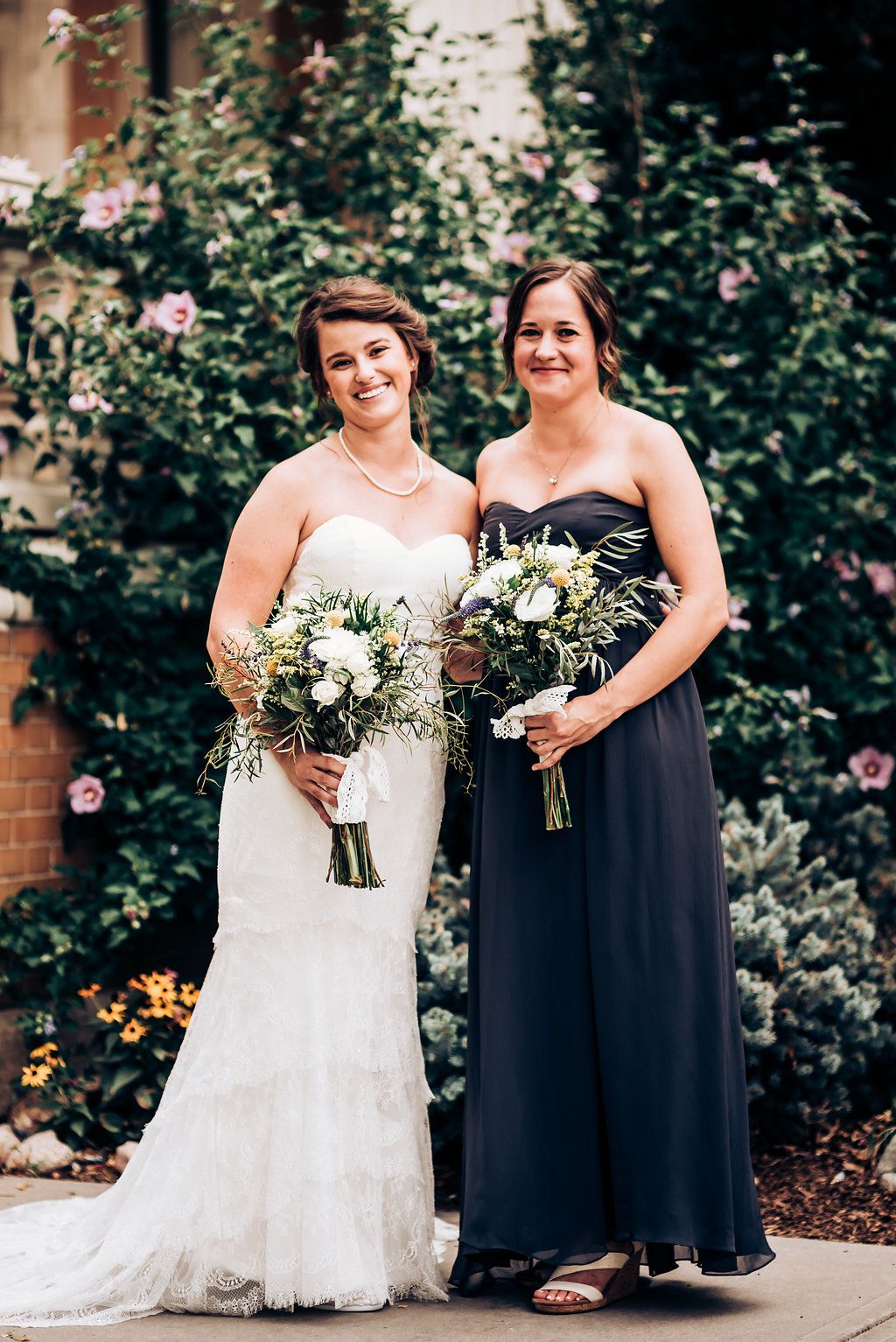 A formal portrait showing two people in contrasting dresses holding elegant white floral bouquets.