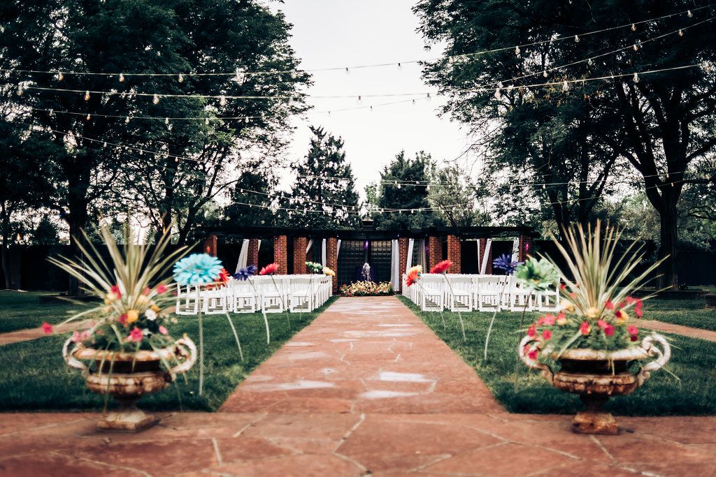 Outdoor wedding ceremony setup with white chairs and decorative plants lining a brick pathway.