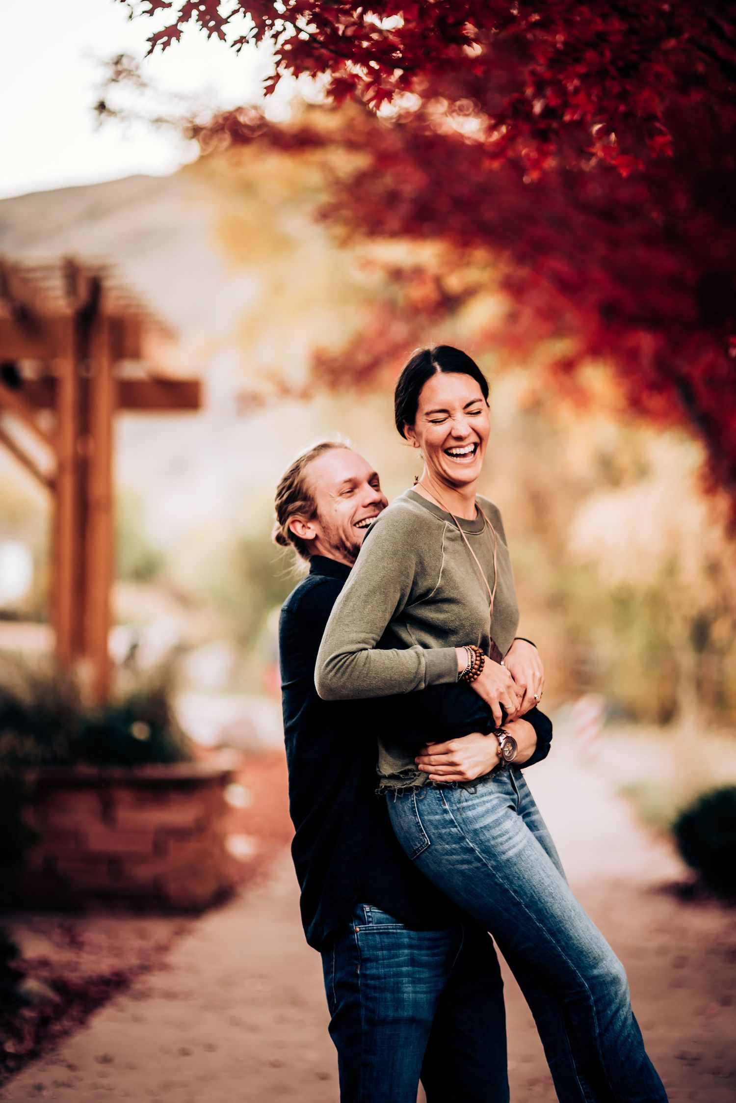 Joyful couple embracing on path under striking red fall foliage.