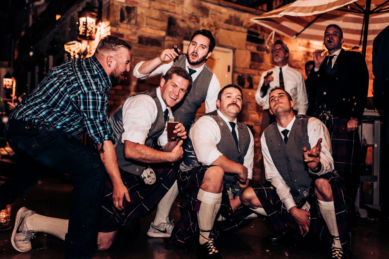 Group of men in traditional German lederhosen and vests posing playfully at an event.
