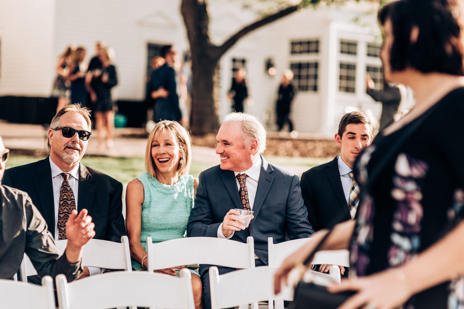 Wedding guests seated at outdoor tables sharing laughs during a daytime reception.