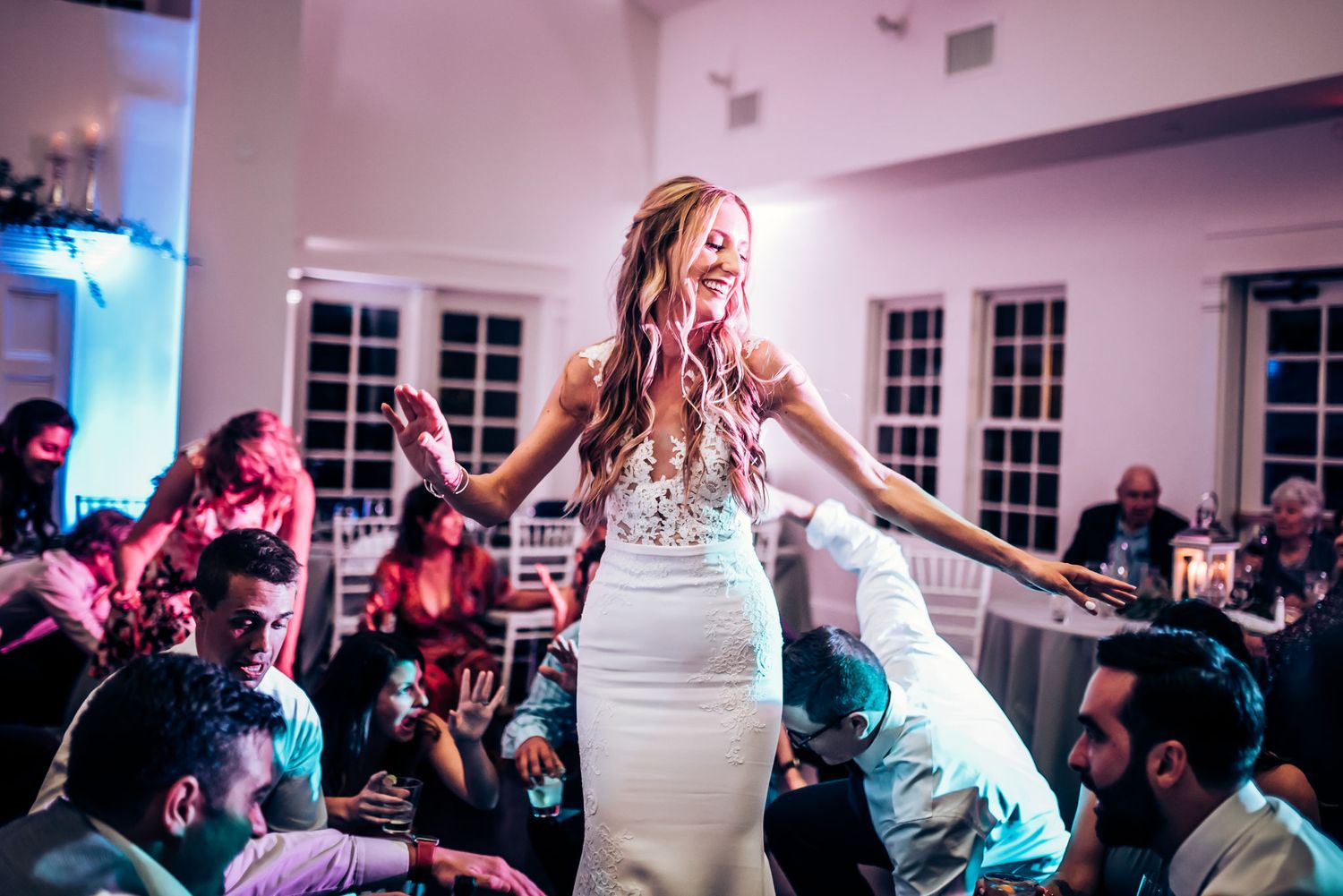 Energetic dance party scene with a white dress in the center of a crowded reception.