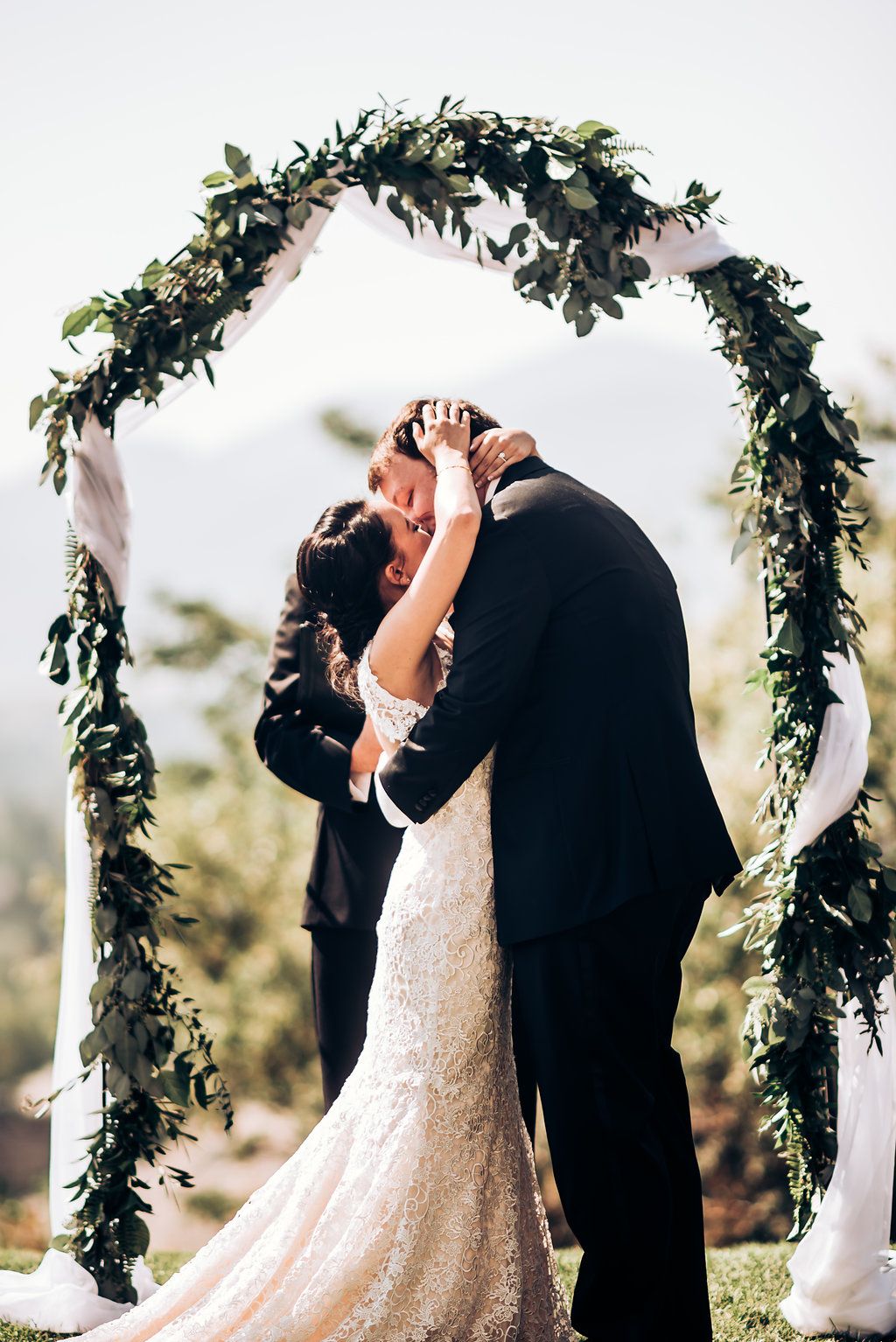 Intimate wedding moment under elegant greenery arch during outdoor ceremony.