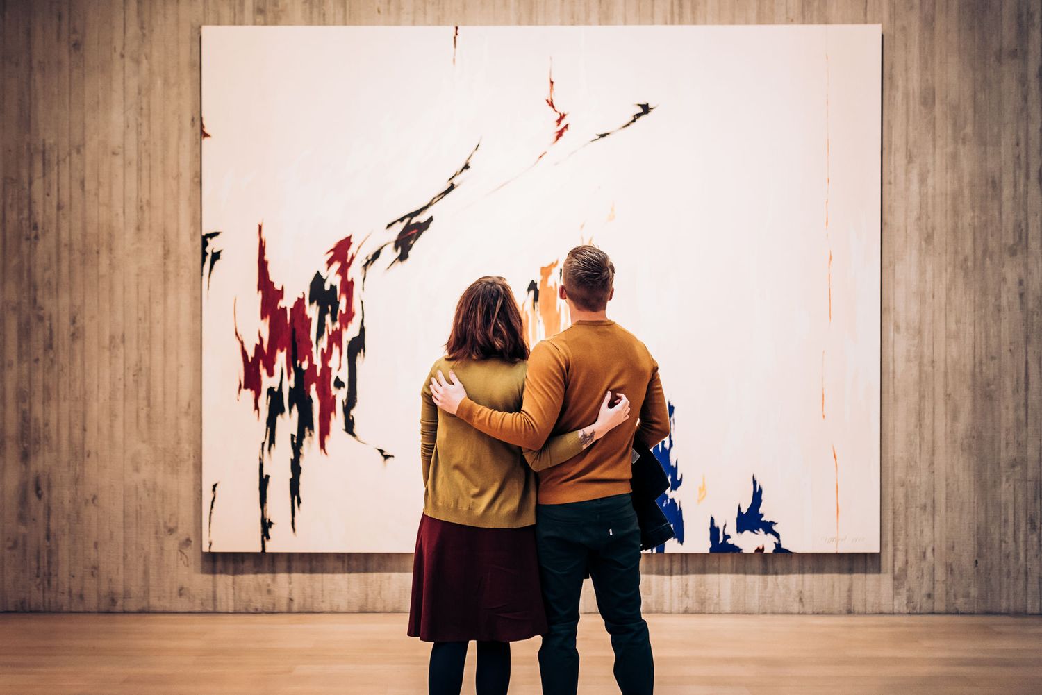 Couple admiring abstract red and black artwork in modern gallery space.