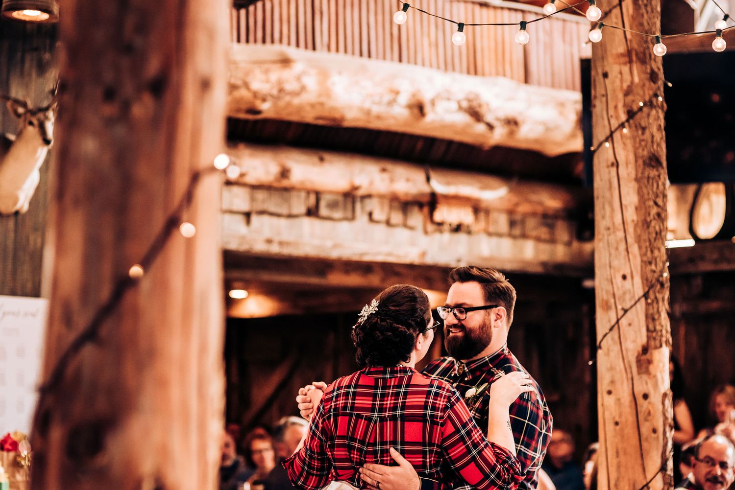 Dancing couple in plaid shirts captured in an intimate moment at a rustic barn venue.