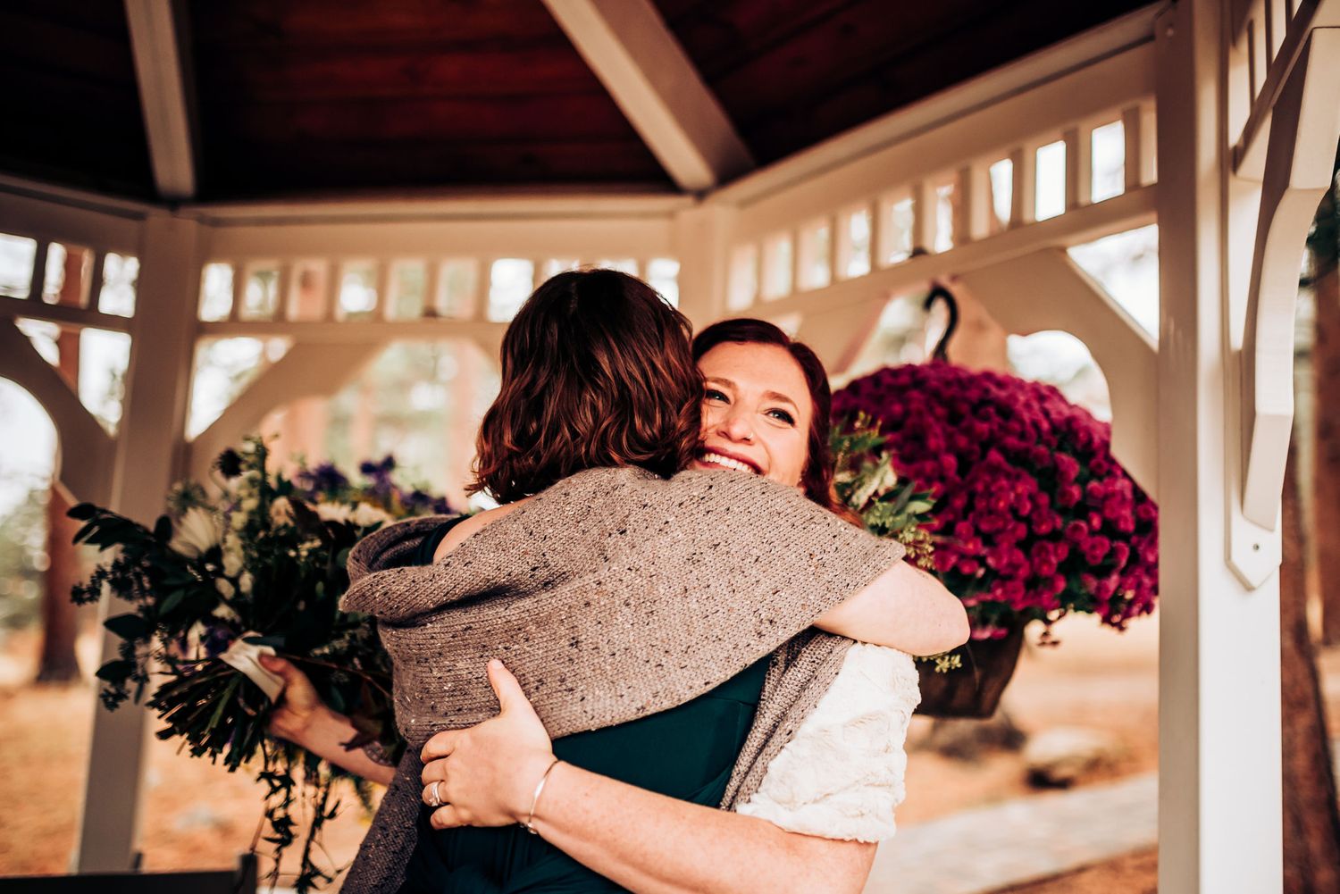 Emotional embrace shared in white wooden gazebo decorated with flowers.