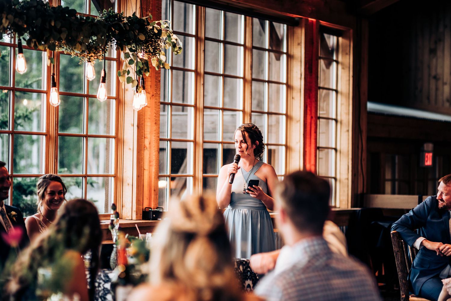 Someone delivers a speech at a reception while guests listen in a rustic venue.