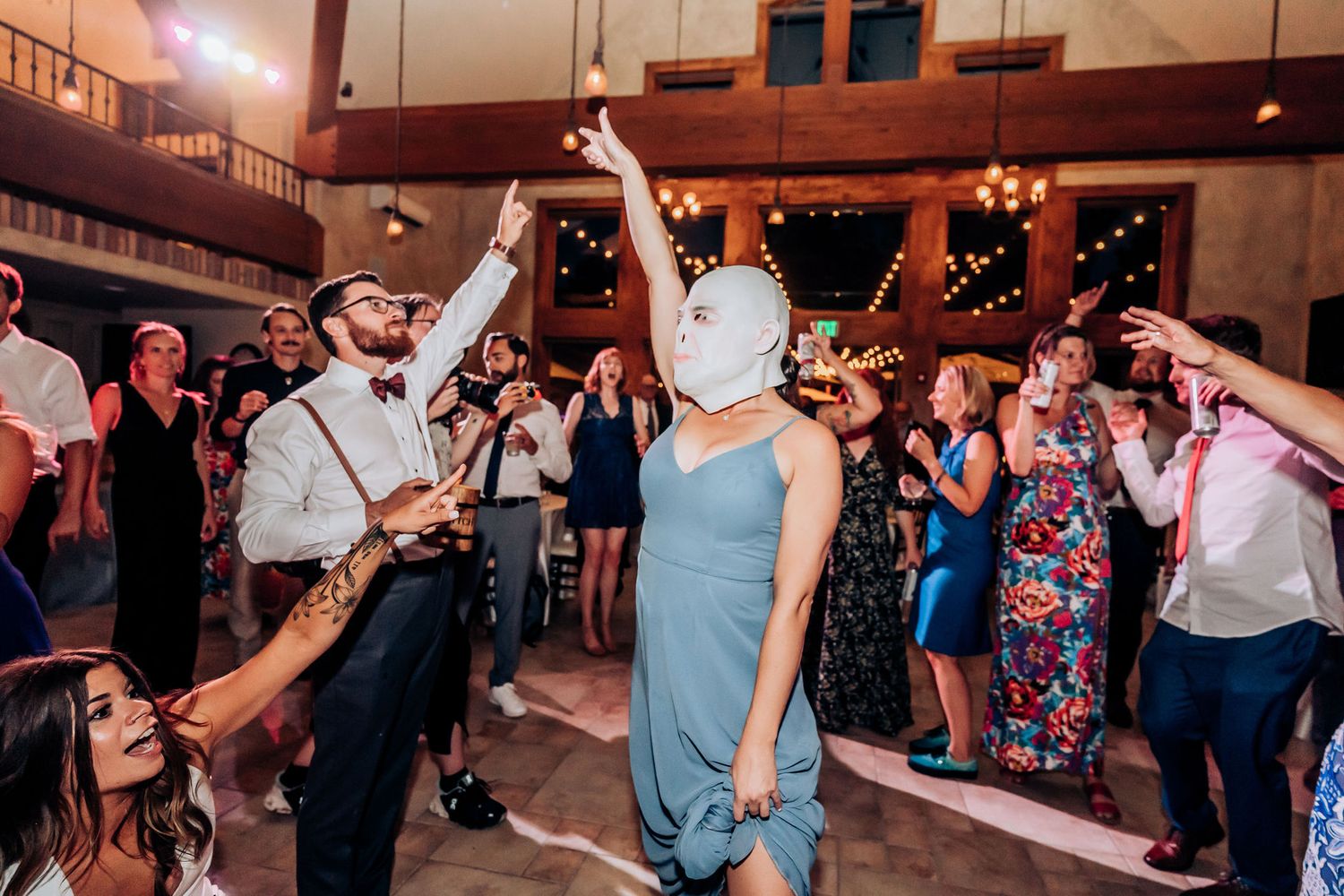 Wedding guests celebrating and dancing under string lights at an indoor reception venue.