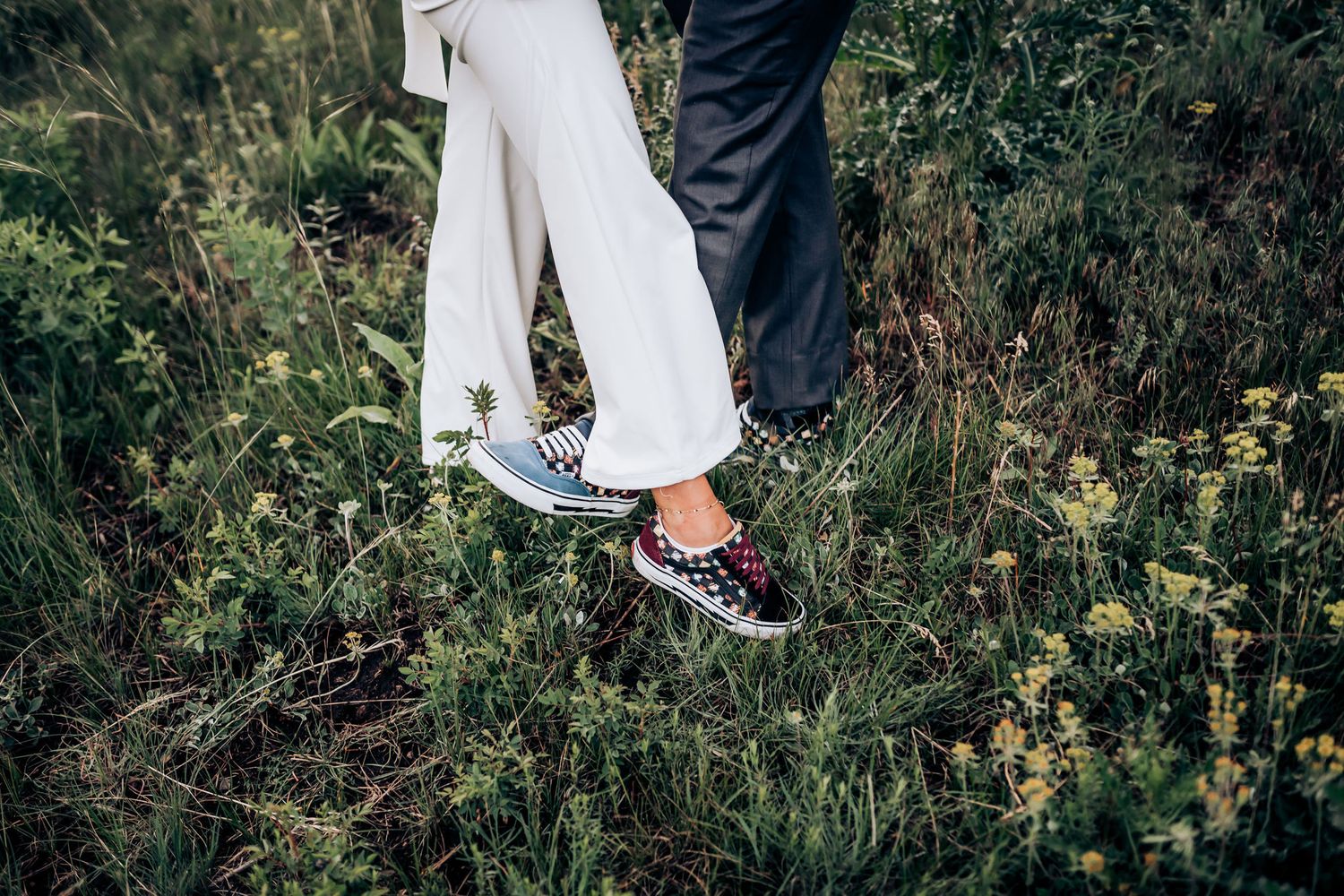 Close-up of bride and groom's feet wearing casual sneakers in a grassy field.