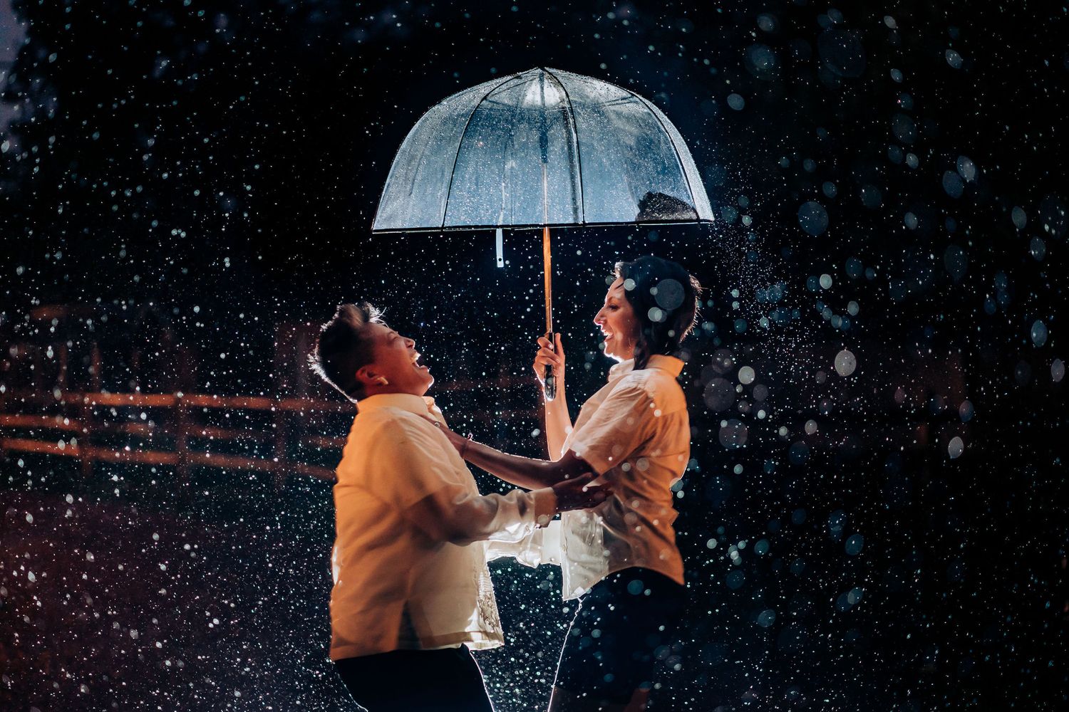 A couple laughs together while sharing an umbrella in the rain at night.