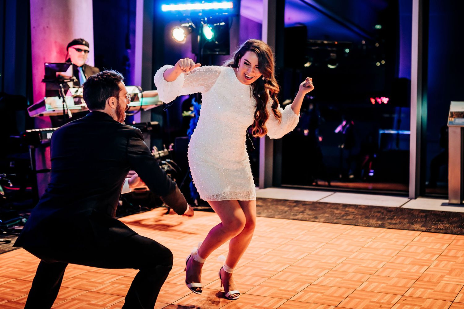 A couple performs a fun dance move on a wooden dance floor during their wedding reception.