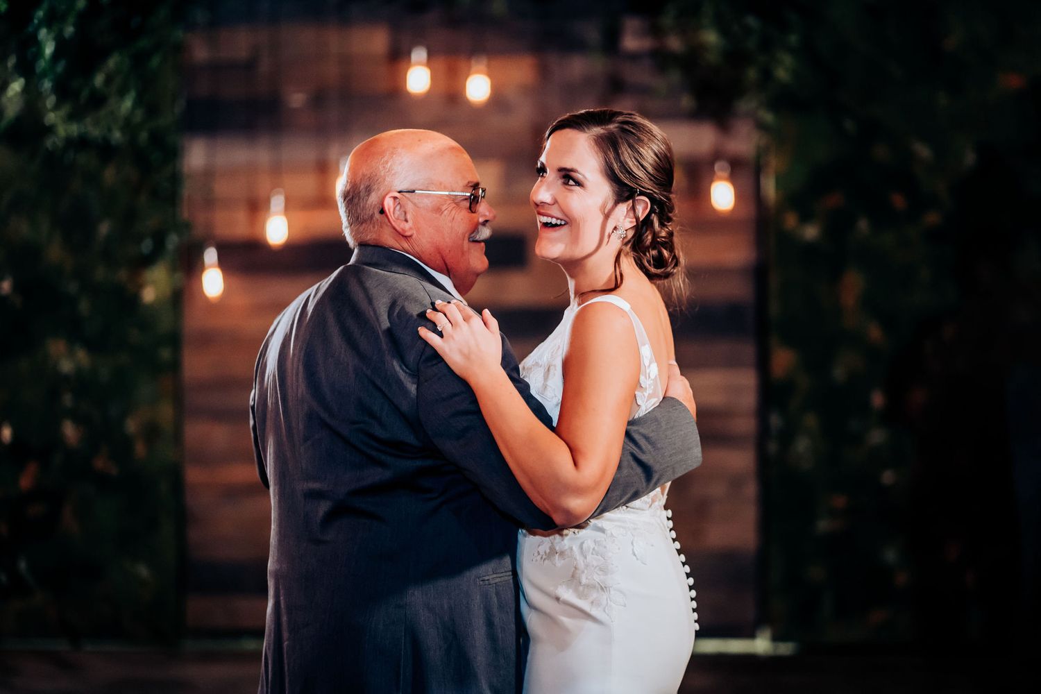 Emotional dance moment captured during wedding reception with romantic string lights and brick backdrop.