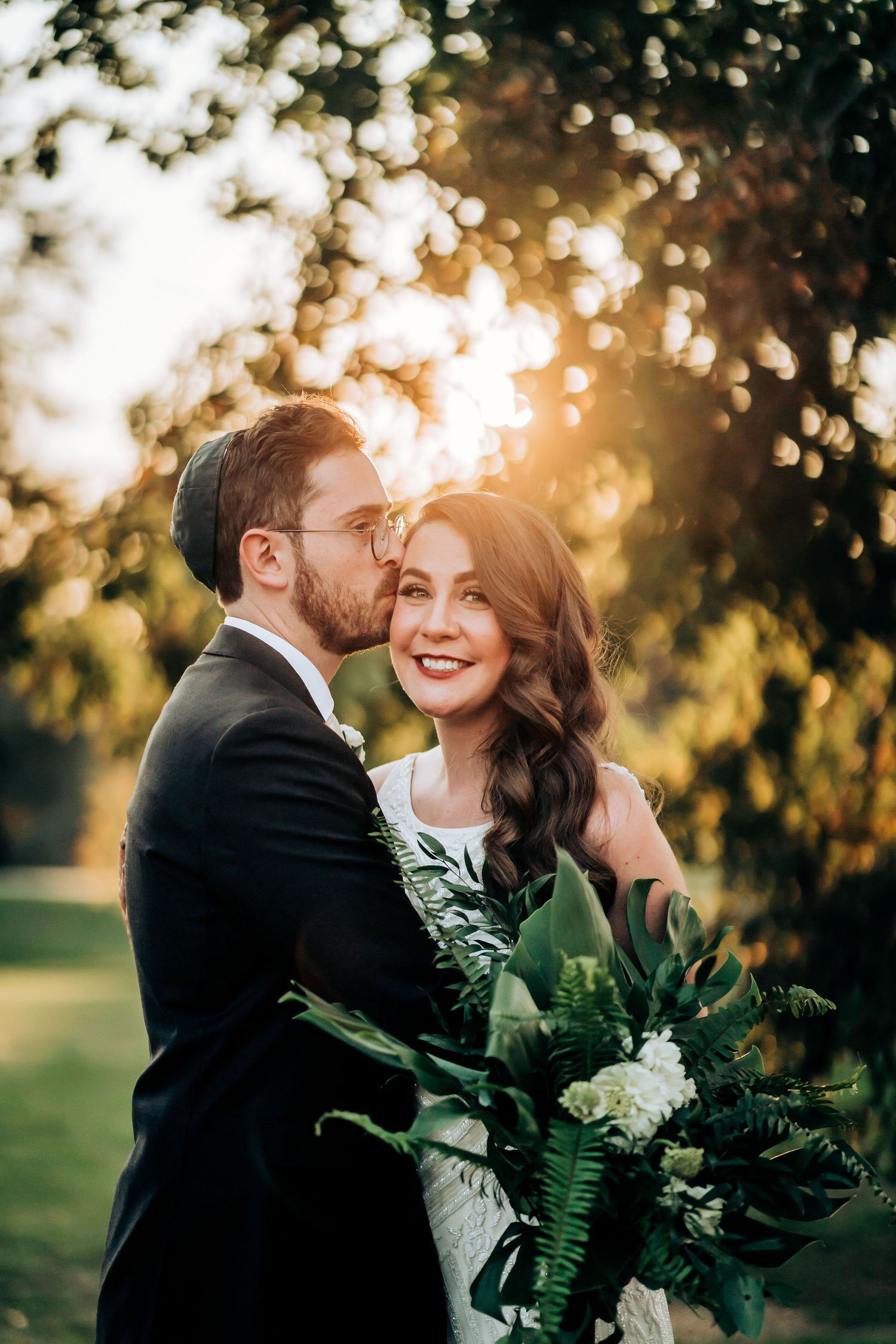 Romantic wedding portrait of a couple sharing an intimate moment at sunset with a greenery bouquet.