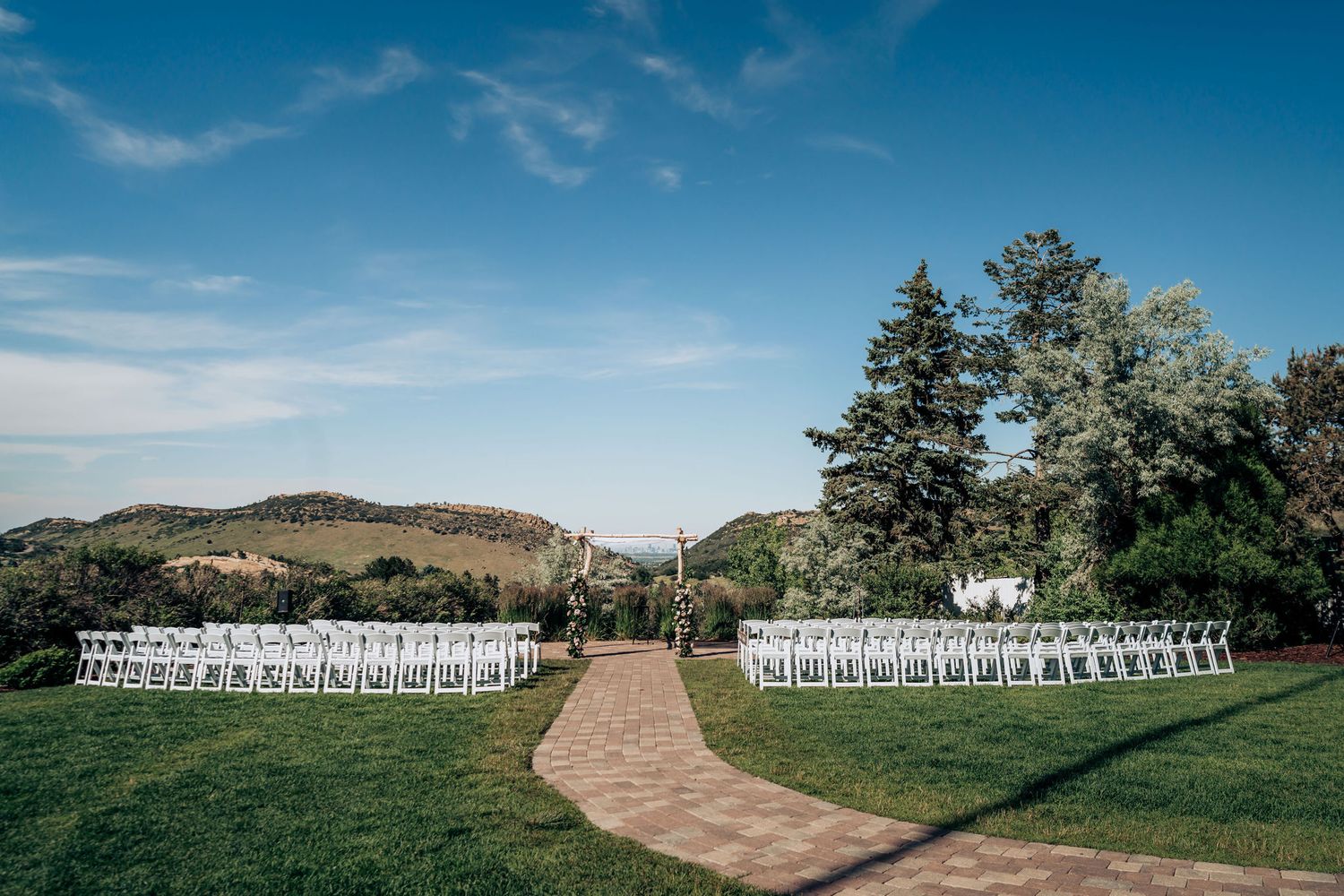 Outdoor wedding ceremony setup with white chairs arranged in rows along a winding path against rolling hills and blue sky.
