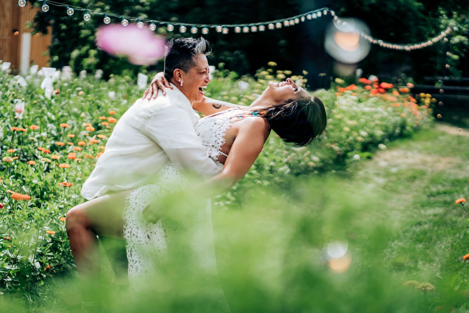 A joyful embrace in a lush garden setting with hanging lights and colorful flowers.