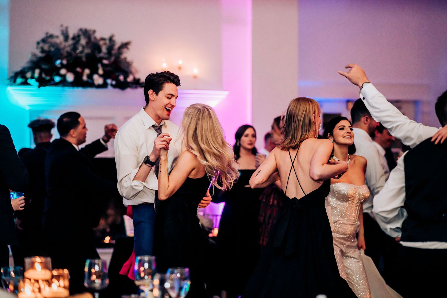 Lively wedding reception dance party with guests dancing and celebrating under purple lighting.