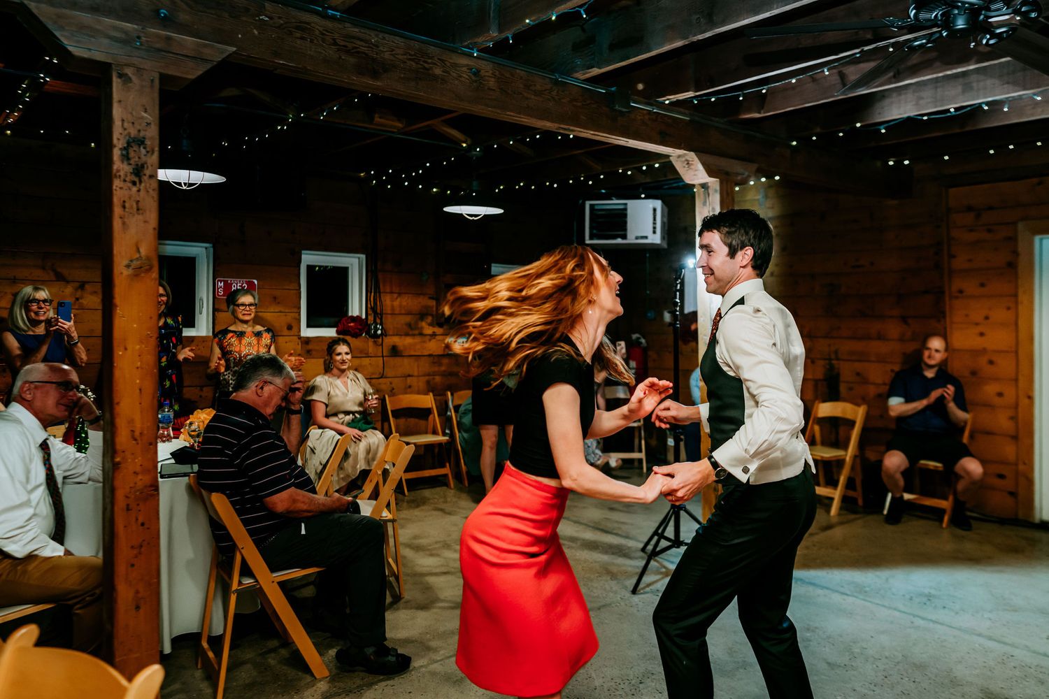 A couple dances energetically in a rustic venue decorated with string lights.